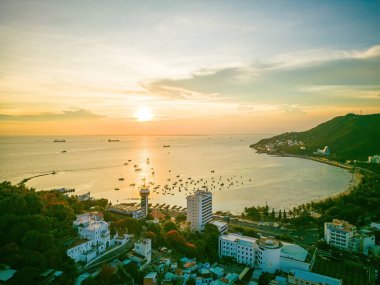 Vung Tau city aerial view with beautiful sunset and so many boats. Panoramic coastal Vung Tau view from above, with waves, coastline, streets, coconut trees and Tao Phung mountain in Vietnam.