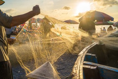Vung Tau, VIETNAM - AUG 20 2022 : Fisherman casting his net at the sunrise or sunset. Traditional fishermen prepare the fishing net. Fishermen on beach at the Fishing.