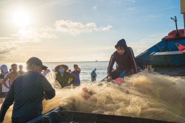 Vung Tau, VIETNAM - AUG 20 2022 : Fisherman casting his net at the sunrise or sunset. Traditional fishermen prepare the fishing net. Fishermen on beach at the Fishing.