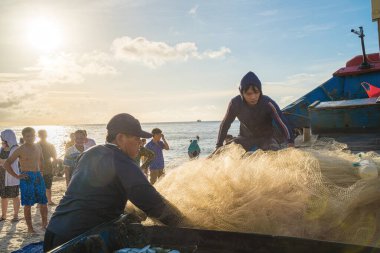 Vung Tau, VIETNAM - AUG 20 2022 : Fisherman casting his net at the sunrise or sunset. Traditional fishermen prepare the fishing net. Fishermen on beach at the Fishing.