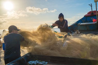 Vung Tau, VIETNAM - AUG 20 2022 : Fisherman casting his net at the sunrise or sunset. Traditional fishermen prepare the fishing net. Fishermen on beach at the Fishing.