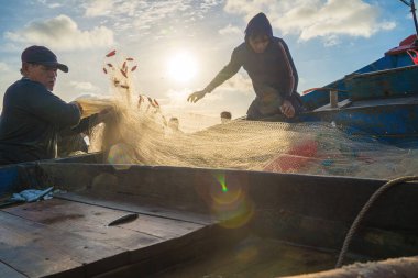 Vung Tau, VIETNAM - AUG 20 2022 : Fisherman casting his net at the sunrise or sunset. Traditional fishermen prepare the fishing net. Fishermen on beach at the Fishing.