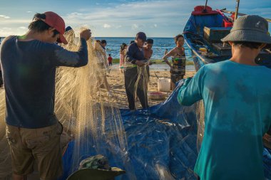 Vung Tau, VIETNAM - AUG 20 2022 : Fisherman casting his net at the sunrise or sunset. Traditional fishermen prepare the fishing net. Fishermen on beach at the Fishing.
