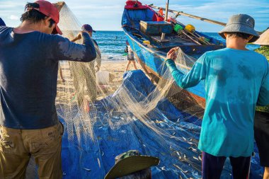 Vung Tau, VIETNAM - AUG 20 2022 : Fisherman casting his net at the sunrise or sunset. Traditional fishermen prepare the fishing net. Fishermen on beach at the Fishing.