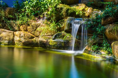 Japanese garden waterfalls. Lush green tropical Koi pond with waterfall from each side. A lush green garden with waterfall cascading down the rocky stones. Zen and peaceful background.