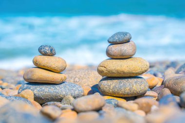 Symbolic scales of stones against the background of the sea and blue sky. Concept of harmony and balance. Pros and cons concept. Pyramid stones balance on the sand of the beach with blurred background