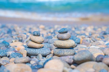 Symbolic scales of stones against the background of the sea and blue sky. Concept of harmony and balance. Pros and cons concept. Pyramid stones balance on the sand of the beach with blurred background