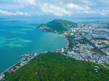 Vung Tau city aerial view with beautiful sunset and so many boats. Panoramic coastal Vung Tau view from above, with waves, coastline, streets, coconut trees and Tao Phung mountain in Vietnam.