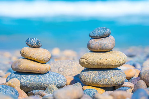 Symbolic scales of stones against the background of the sea and blue sky. Concept of harmony and balance. Pros and cons concept. Pyramid stones balance on the sand of the beach with blurred background