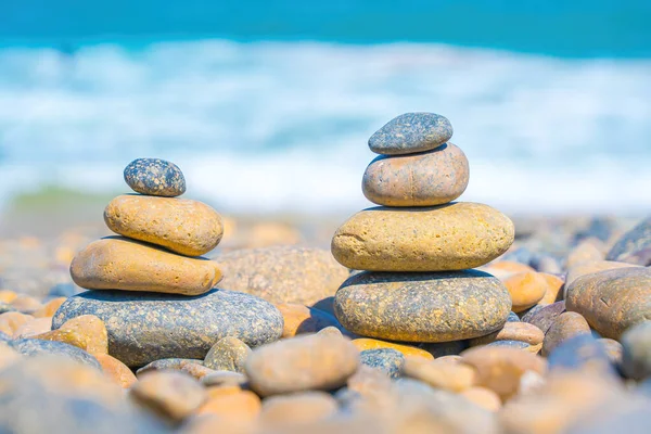 Symbolic scales of stones against the background of the sea and blue sky. Concept of harmony and balance. Pros and cons concept. Pyramid stones balance on the sand of the beach with blurred background