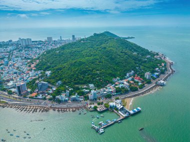 Vung Tau city aerial view with beautiful sunset and so many boats. Panoramic coastal Vung Tau view from above, with waves, coastline, streets, coconut trees and Tao Phung mountain in Vietnam.