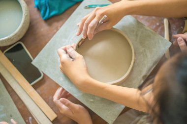 Top view Woman potter working on potters wheel making ceramic pot from clay in pottery workshop. Focus hand young woman attaching clay product part to future ceramic product. Pottery workshop.