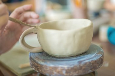 Woman potter working on potters wheel making ceramic pot from clay in pottery workshop. art concept. Focus hand young woman attaching clay product part to future ceramic product. Pottery workshop.