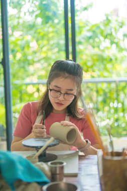 Beautiful woman potter working on potters wheel making ceramic pot from clay in pottery workshop. Focus hand young woman attaching clay product part to future ceramic product. Pottery workshop.