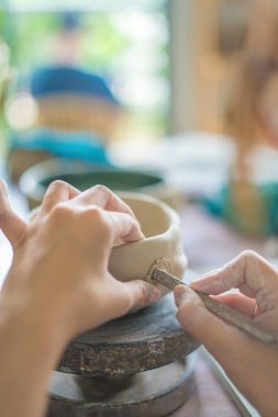 Woman potter working on potters wheel making ceramic pot from clay in pottery workshop. art concept. Focus hand young woman attaching clay product part to future ceramic product. Pottery workshop.