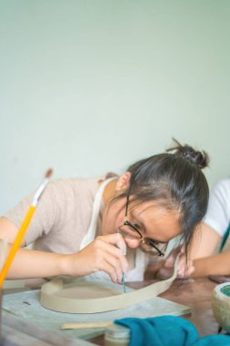 Beautiful woman potter working on potters wheel making ceramic pot from clay in pottery workshop. Focus hand young woman attaching clay product part to future ceramic product. Pottery workshop.