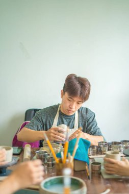 Man potter working on potters wheel making ceramic pot from clay in pottery workshop. art concept. Focus hand young man attaching clay product part to future ceramic product. Pottery workshop.