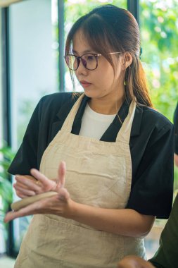 Beautiful woman potter working on potters wheel making ceramic pot from clay in pottery workshop. Focus hand young woman attaching clay product part to future ceramic product. Pottery workshop.