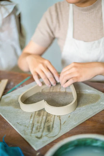 Woman potter working on potters wheel making ceramic pot from clay in pottery workshop. art concept. Focus hand young woman attaching clay product part to future ceramic product. Pottery workshop.