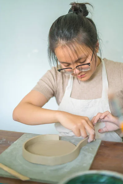 Beautiful woman potter working on potters wheel making ceramic pot from clay in pottery workshop. Focus hand young woman attaching clay product part to future ceramic product. Pottery workshop.