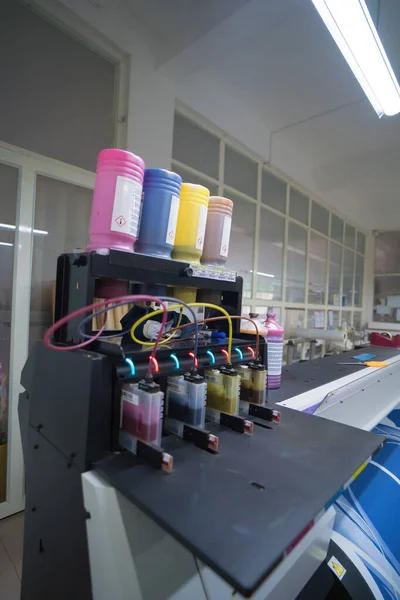 Close up CMYK ink bottles from a sublimation printer. Interior factory Large printing machine for paper business in printing room. Sublimation concept.