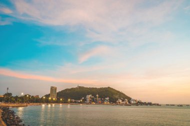 Vung Tau city aerial view with beautiful sunset and so many boats. Panoramic coastal Vung Tau view from above, with waves, coastline, streets, coconut trees and Tao Phung mountain in Vietnam.