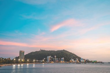 Vung Tau city aerial view with beautiful sunset and so many boats. Panoramic coastal Vung Tau view from above, with waves, coastline, streets, coconut trees and Tao Phung mountain in Vietnam.