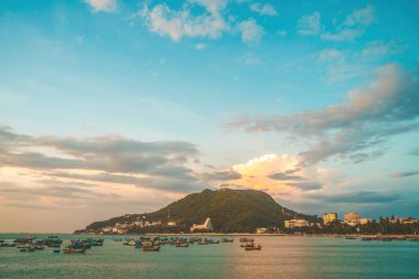 Vung Tau city aerial view with beautiful sunset and so many boats. Panoramic coastal Vung Tau view from above, with waves, coastline, streets, coconut trees and Tao Phung mountain in Vietnam.