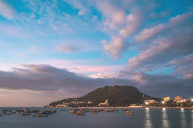 Vung Tau city aerial view with beautiful sunset and so many boats. Panoramic coastal Vung Tau view from above, with waves, coastline, streets, coconut trees and Tao Phung mountain in Vietnam.