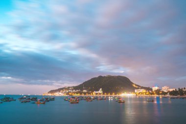 Vung Tau city aerial view with beautiful sunset and so many boats. Panoramic coastal Vung Tau view from above, with waves, coastline, streets, coconut trees and Tao Phung mountain in Vietnam.