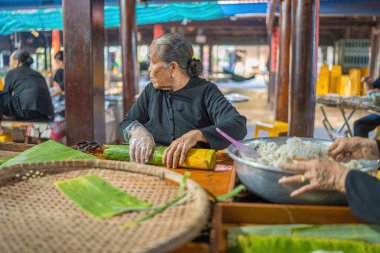 Vung Tau, VIETNAM - JAN 12 2023: Focus old woman with traditional Vietnamese dress (ao ba ba) Making (wrapping) Tet Cake, the Vietnamese lunar new year Tet food outdoor by hands.