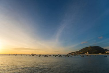 Vung Tau city aerial view with beautiful sunset and so many boats. Panoramic coastal Vung Tau view from above, with waves, coastline, streets, coconut trees and Tao Phung mountain in Vietnam.
