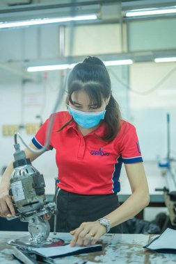 Ba Ria, VIETNAM - JAN 19 2023: Focus woman with cutter machine and personal protective equipment at garment industrial work place. Fabric cutter in Asian textile garment factory
