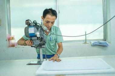 Ba Ria, VIETNAM - JAN 19 2023: Man with cutter machine and personal protective equipment at garment industrial work place. Fabric cutter in Asian textile garment factory