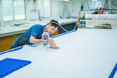 Ba Ria, VIETNAM - JAN 19 2023: Man with cutter machine and personal protective equipment at garment industrial work place. Fabric cutter in Asian textile garment factory