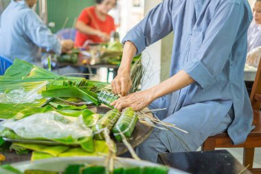 Focus old woman with traditional Vietnamese dress (ao ba ba) Making (wrapping) Tet Cake, the Vietnamese lunar new year Tet food outdoor by hands.