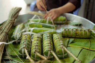 Focus old woman with traditional Vietnamese dress (ao ba ba) Making (wrapping) Tet Cake, the Vietnamese lunar new year Tet food outdoor by hands.