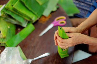 Focus old woman with traditional Vietnamese dress (ao ba ba) Making (wrapping) Tet Cake, the Vietnamese lunar new year Tet food outdoor by hands.