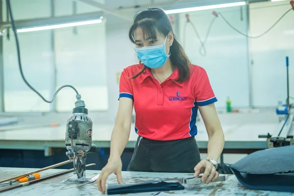 Ba Ria, VIETNAM - JAN 19 2023: Focus woman with cutter machine and personal protective equipment at garment industrial work place. Fabric cutter in Asian textile garment factory