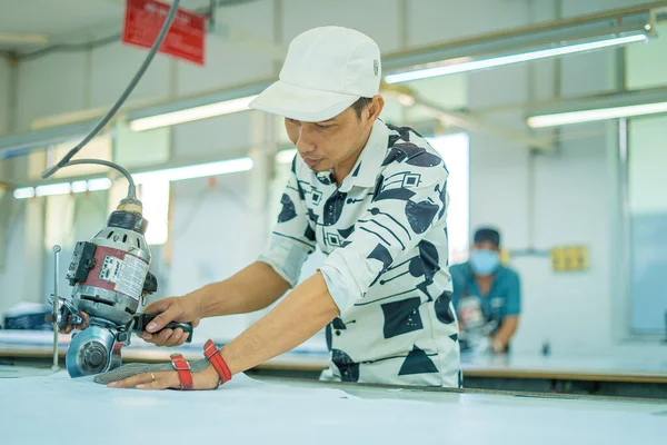 Ba Ria, VIETNAM - JAN 19 2023: Man with cutter machine and personal protective equipment at garment industrial work place. Fabric cutter in Asian textile garment factory