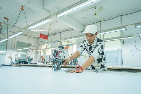 Ba Ria, VIETNAM - JAN 19 2023: Man with cutter machine and personal protective equipment at garment industrial work place. Fabric cutter in Asian textile garment factory