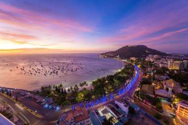 Vung Tau city aerial view with beautiful sunset and so many boats. Panoramic coastal Vung Tau view from above, with waves, coastline, streets, coconut trees and Tao Phung mountain in Vietnam.
