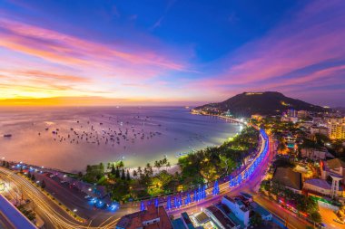 Vung Tau city aerial view with beautiful sunset and so many boats. Panoramic coastal Vung Tau view from above, with waves, coastline, streets, coconut trees and Tao Phung mountain in Vietnam.