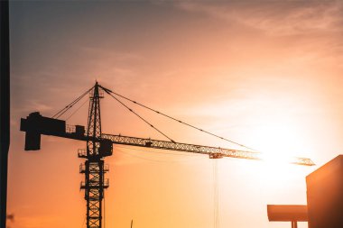 Silhouette Construction crane on the background of the sky sunset. Construction site. Large construction site including several cranes working on a building complex, with clear yellow sky and the sun