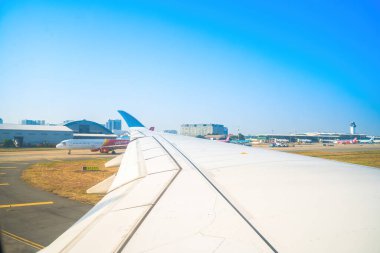 Havaalanının penceresinden Tan Son Nhat 'i izleyin. Mavi gökyüzü ve uçak penceresi manzaralı tüylü beyaz bulutlar, jet motoru kanatta. Uçak bileti rezervasyonu. Pencere kenarı. Seçici odak