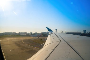 Havaalanının penceresinden Tan Son Nhat 'i izleyin. Mavi gökyüzü ve uçak penceresi manzaralı tüylü beyaz bulutlar, jet motoru kanatta. Uçak bileti rezervasyonu. Pencere kenarı. Seçici odak
