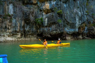 Ha Long, VİETNAM MAR 12 2023: Ha Long Körfezi 'ndeki kireçtaşı kayaların arasında yüzen turist hurdaları, Halong Körfezi, Vietnam yakınlarındaki Lan Ha Körfezi' ndeki bir mağarada kano yapan insanlar.