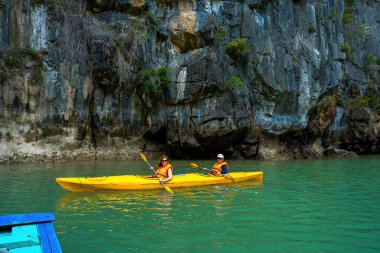 Ha Long, VİETNAM MAR 12 2023: Ha Long Körfezi 'ndeki kireçtaşı kayaların arasında yüzen turist hurdaları, Halong Körfezi, Vietnam yakınlarındaki Lan Ha Körfezi' ndeki bir mağarada kano yapan insanlar.