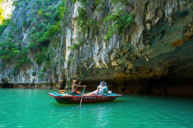 Ha Long, VIETNAM MAR 12 2023: Tourist junks floating among limestone rocks at Ha Long Bay, people kayaking inside of a cave in Lan Ha Bay, close to Halong Bay, Vietnam clipart
