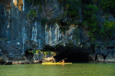 Ha Long, VİETNAM MAR 12 2023: Ha Long Körfezi 'ndeki kireçtaşı kayaların arasında yüzen turist hurdaları, Halong Körfezi, Vietnam yakınlarındaki Lan Ha Körfezi' ndeki bir mağarada kano yapan insanlar.